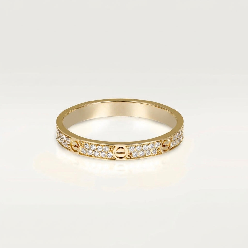 A gold ring with pavé-set clear stones and screw-like details, photographed on a clean light gray background.
