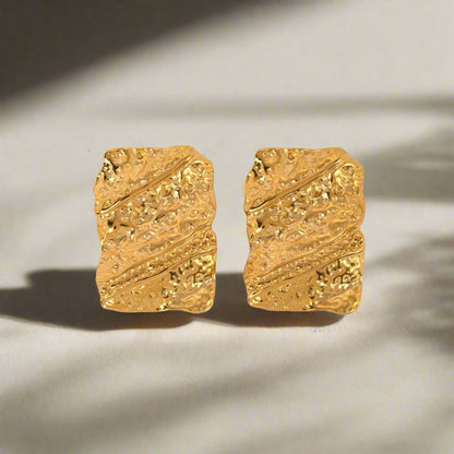 two gold earrings laying flat on a surface